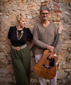 Un uomo e una donna con chitarre accanto a un muro di pietra.
